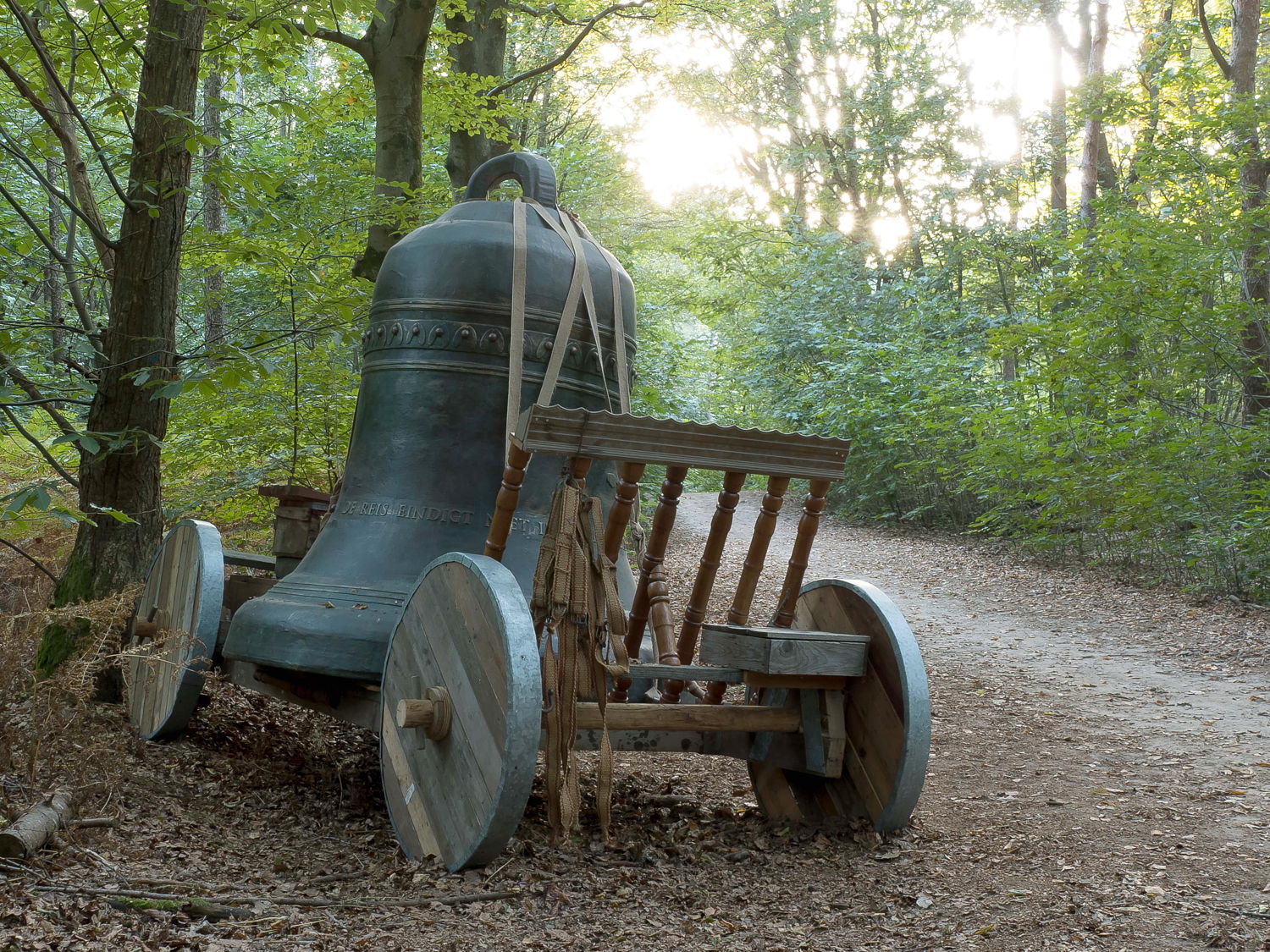 Grote bronzen kerkklok op gammele kar langs de rand van de weg. Titel: De Reis eindigt niet in Eden